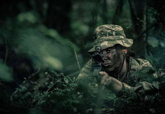 Private Zara Reid looks down the scope of a rifle in full camouflage as she takes part in regular training with Wellington Company, 5/7 Battalion, RNZIR