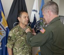 A man in military uniforn receives the Legion of Merit from an Admiral with a United States flag on their arm.