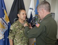 A man in military uniforn receives the Legion of Merit from an Admiral with a United States flag on their arm.