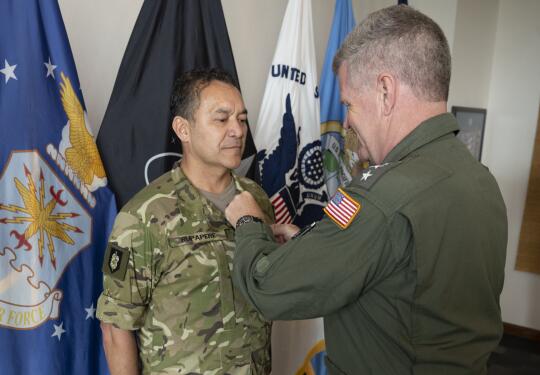 A man in military uniforn receives the Legion of Merit from an Admiral with a United States flag on their arm.