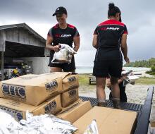 Three people move goods from the back of truck, each wearing New Zealand Army t-shirts and New Zealand Defence Force caps.