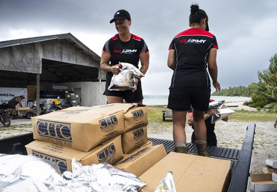 Three people move goods from the back of truck, each wearing New Zealand Army t-shirts and New Zealand Defence Force caps.