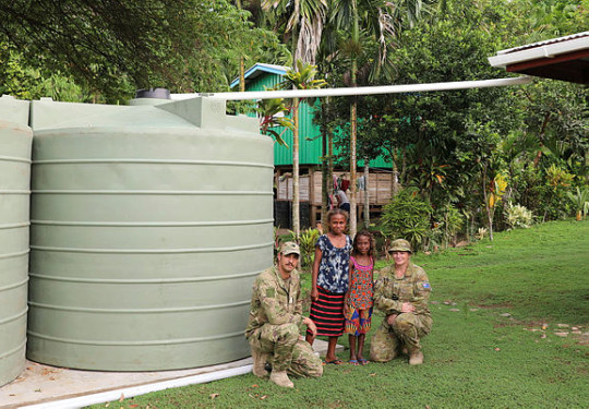 Lieutenant Mitchell Berryman (NZDF) and Lieutenant Lisa Thwaites (ADF) with children of the Bloody Ridge community and their new water tanks. 
