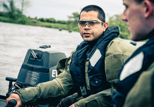 Soldier with lifejacket and protective glasses controls the small boat they are aboard.