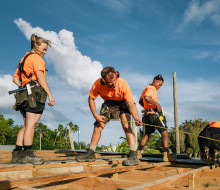 NZ Army personnel wearing orange high visibility shirts carry out construction work under blue skies.