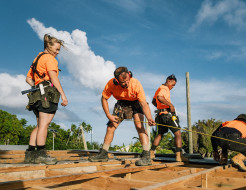 NZ Army personnel wearing orange high visibility shirts carry out construction work under blue skies.