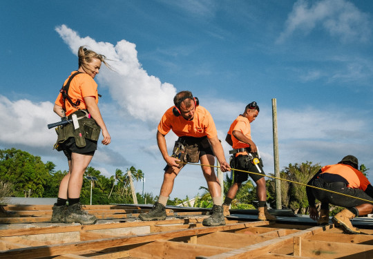 NZ Army personnel wearing orange high visibility shirts carry out construction work under blue skies.