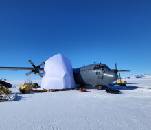A grey aircraft on the ice in Antarctica. The aircraft has a white box around the right wing.