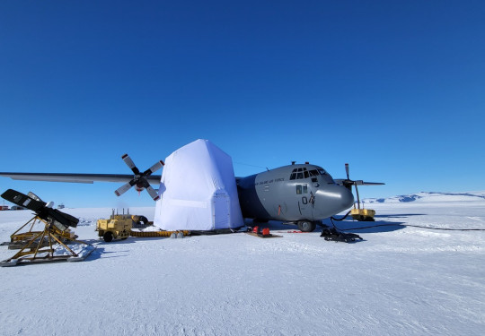 A grey aircraft on the ice in Antarctica. The aircraft has a white box around the right wing.