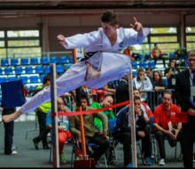 A man conducts a Taekwon-Do jumping kick while wearing a the white Taekwon-Do uniform and a black belt.