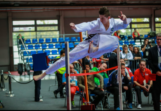 A man conducts a Taekwon-Do jumping kick while wearing a the white Taekwon-Do uniform and a black belt.