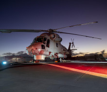 Seasprite helicopter on the deck of HMNZS Otago lit by red lights in the early morning light.