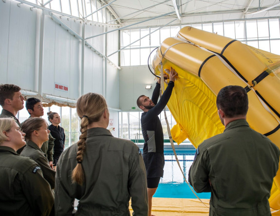 Aircrew at a swimming pool receive a demonstration on an inflatable boat during a training session around fundamental survival skills .