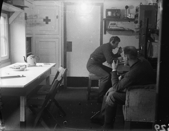 Two coastwatchers, one of whom is manning the radio, in a hut on Auckland Islands in 1942. Credit: Alexander Turnbull Library, Fleming, Lady :Glass negatives taken by Sir Charles Fleming on the Auckland Islands in 1942, 1/4-066868-G.