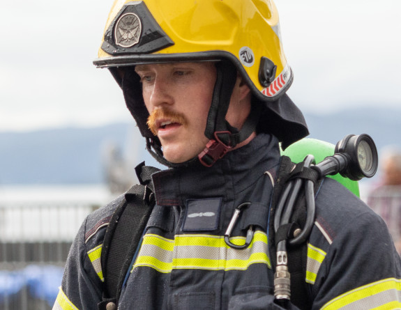 A firefighter wearing a yellow helmet and oxygen tank takes some deep breaths after running the course. 