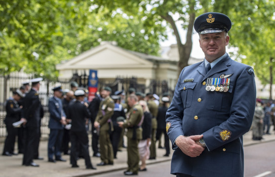 Warrant Officer Paul Chadwick in Air Force uniform standing in front of the various contingents under the green trees of Summer.