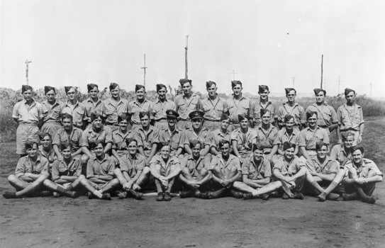 A historical black and white photo of three rows of people in Guadalcanal in 1943.