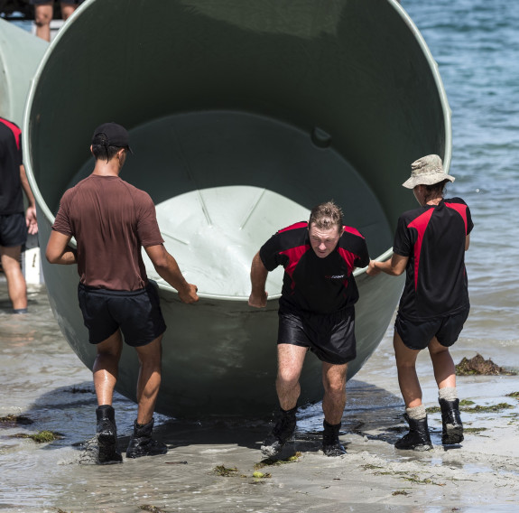 Three New Zealand soldiers carry a water tank off the shore and onto a beach in Fiji