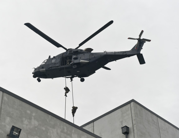 Nh90 helicopter hovers over the new Battle Training Facility with personnel rapelling down ropes from the helicopter.