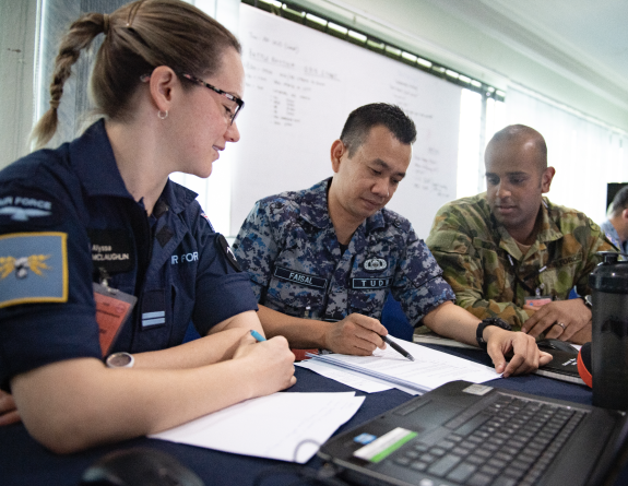 One of our Air Force personnel engage with personnel from foreign militaries at a desk during a multinational exercise.