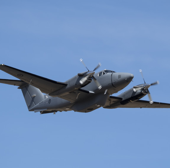 Low angle, mid-shot of the small grey King Air aircraft in front of clear blue sky.