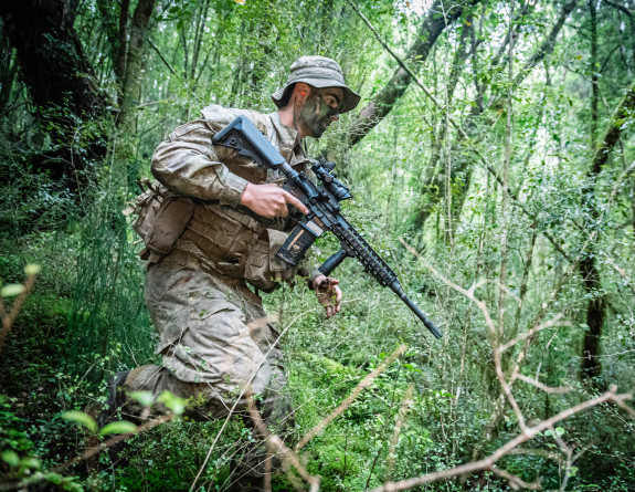 A soldier navigates through dense bush while holding a MARS-L rifle