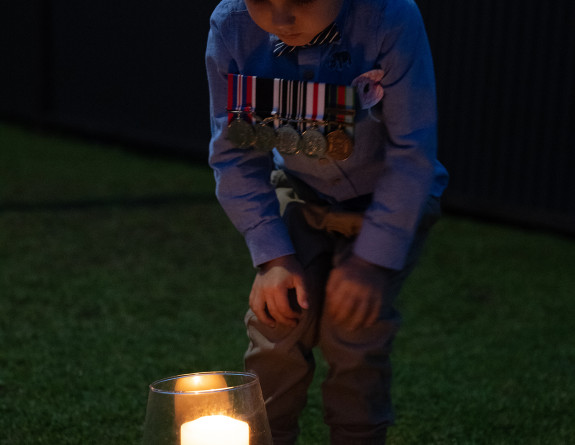 A child looking at two candles in their backyard while wearing their relatives medals during Stand at Dawn 2020