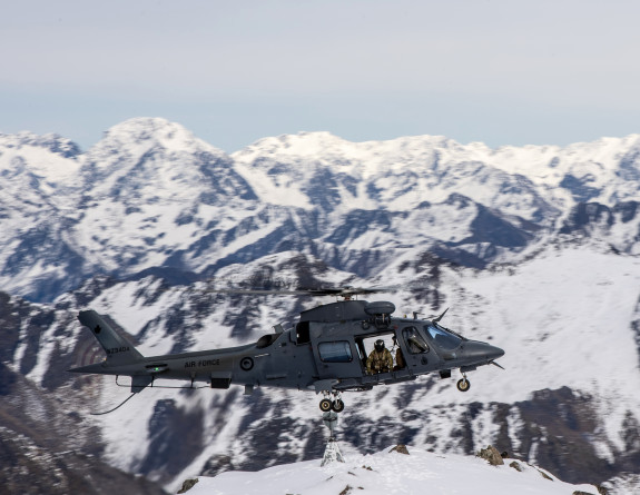 An A109 helicopter hovering over a snow capped mountains