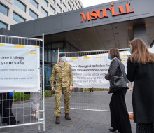 A soldier stands guard at a managed isolation facility and engages with returnees at a safe distance