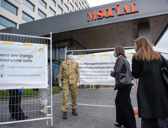 A soldier stands guard at a managed isolation facility and engages with returnees at a safe distance