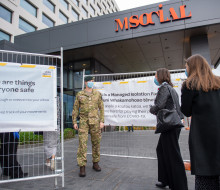 A soldier stands guard at a managed isolation facility and engages with returnees at a safe distance