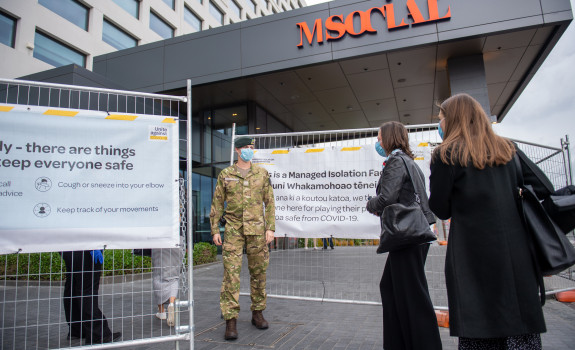 A soldier stands guard at a managed isolation facility and engages with returnees at a safe distance