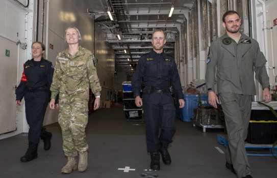 Personnel on board HMNZS Canterbury wearing different uniforms walk through the aircraft hangar