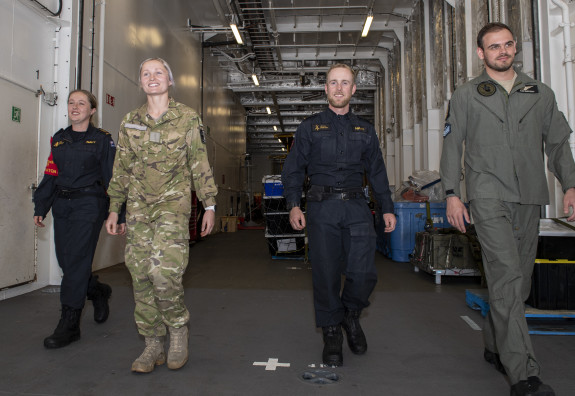 Personnel on board HMNZS Canterbury wearing different uniforms walk through the aircraft hangar