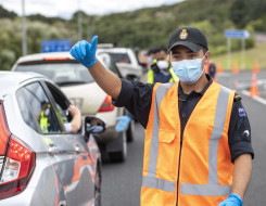 A navy sailor wearing high vis and a mask gives the thumbs up to a vehicle during a checkpoint inspection in Auckland