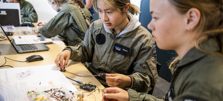 Two School to Skies participants work in flight suits work together to assemble small parts