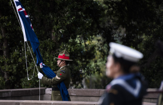 A New Zealand Army soldier lowers a flag during the last post at an Anzac Day service in 2021