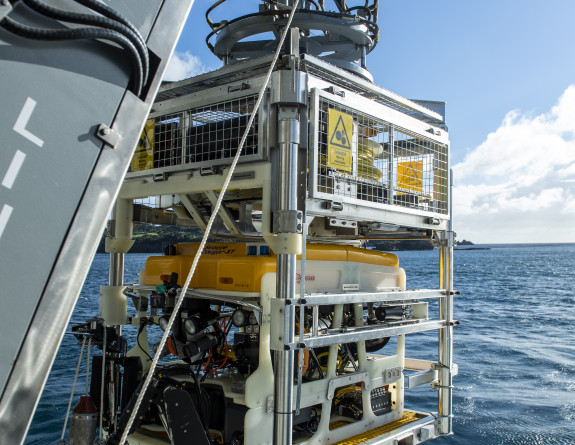 HMNZS Manawanui’s remotely operated vehicle is suspended by crane over the ocean, ready to be launched.