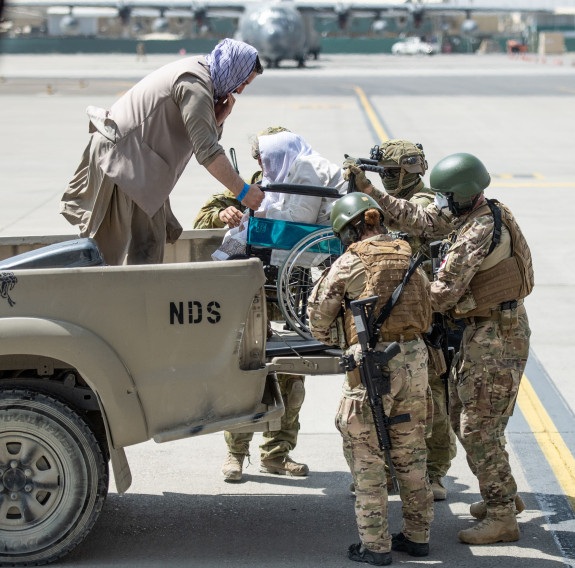 Four NZDF personnel help get an evacuee in a wheelchair get off a truck