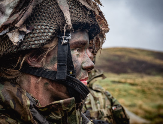 Private Leah Miles in full camouflage uniform, including a helmet and face paint in the field.