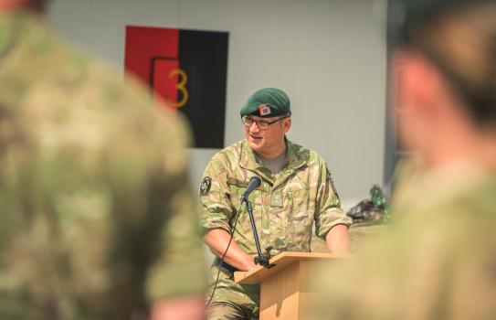 Commanding Officer 3CSSB, Lieutenant Colonel Marcus Linehan stands at a podium in uniform while addressing the unit during the ceremony