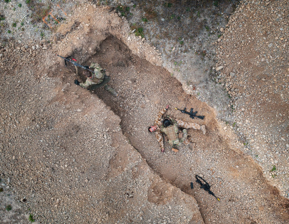 A birds eye view of a trench. One soldier covers the other two, one providing medical aid to the other.
