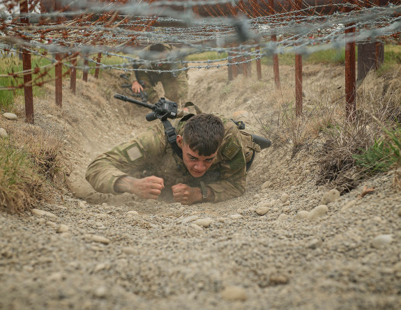 A soldier crawls under barbed wire during Exercise Foxhound