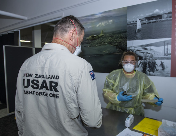 A member of Fire and Emergency New Zealand prepares to board their flight to Papua New Guinea. They are going through health protocols with a person opposite them. 