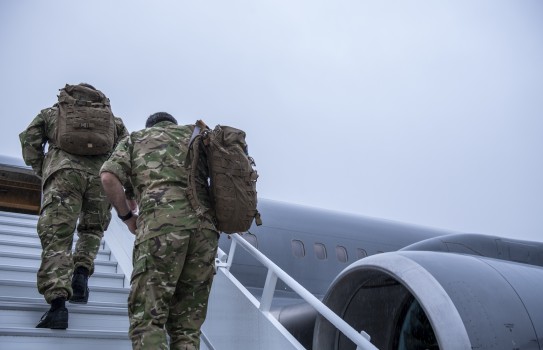 New Zealand Army personnel in uniform walk up the stars towards a Royal New Zealand Air Force Boeing aircraft. The sky is grey and it's a darker image. 