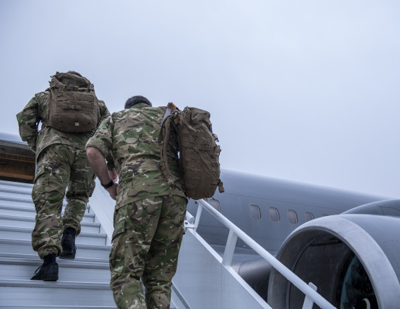 New Zealand Army personnel in uniform walk up the stars towards a Royal New Zealand Air Force Boeing aircraft. The sky is grey and it's a darker image. 