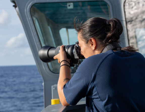 A sailor looks out over the ocean through a camera.