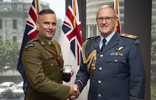 Major Soren Hall and the Chief of Defence Force Air Marshal Kevin Short shake hands - in the background three flags