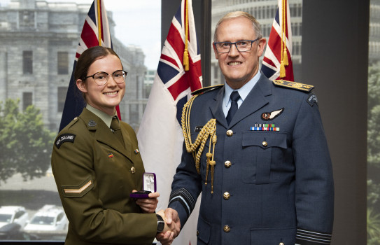 Lance Corporal Erica Campbell and the Chief of Defence Force Air Marshal Kevin Short shake hands - in the background three flags