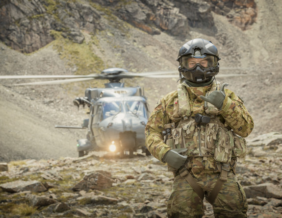 A Helicopter Loadmaster stands in front of an NH90 helicopter. The HLM is pulling a shacka.